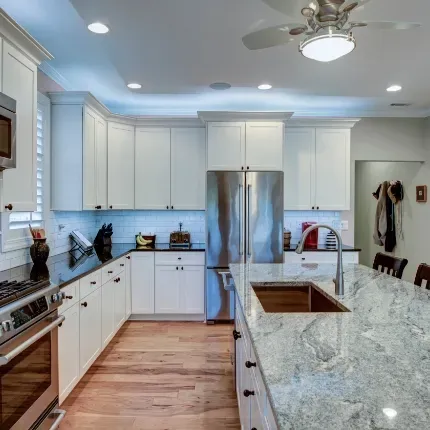 Non-porous granite countertops in an all white kitchen with real wood floors and stainless steel appliances.